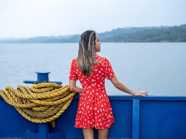A woman in a red dress looking out over the water from a boat.