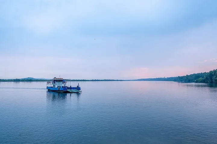 A ferry boat crossing a wide river under a cloudy blue sky.